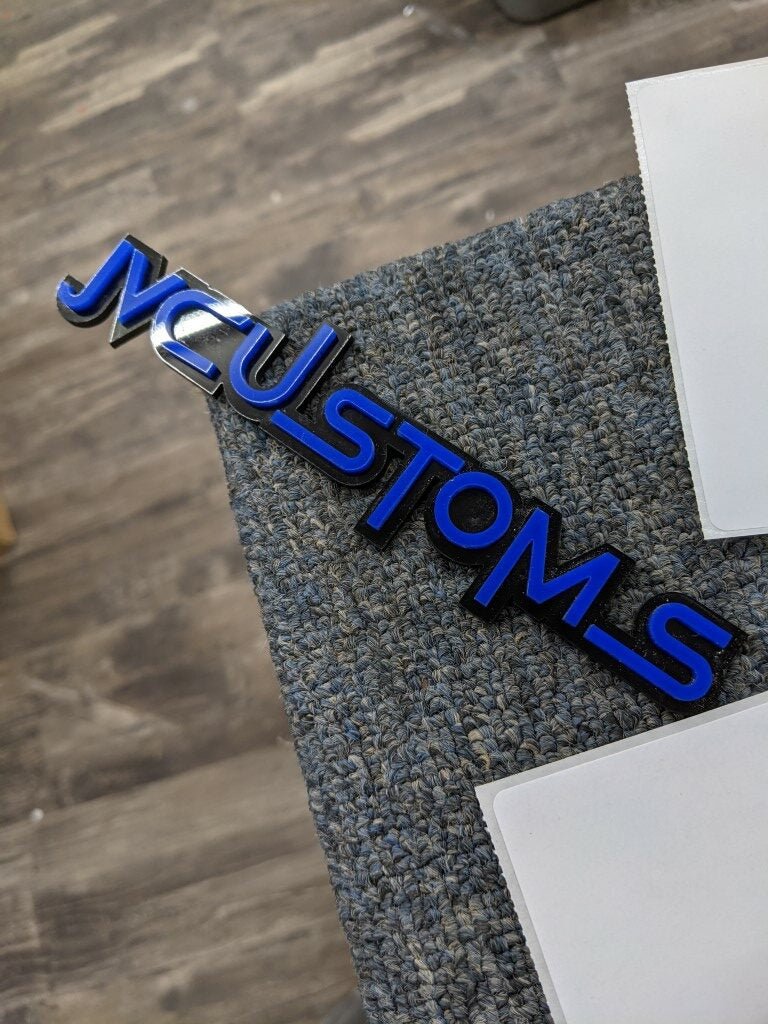 JVCustoms Car Badge - Blue On Gloss Black - Squid Font - Tape Mount - Atomic Car Concepts