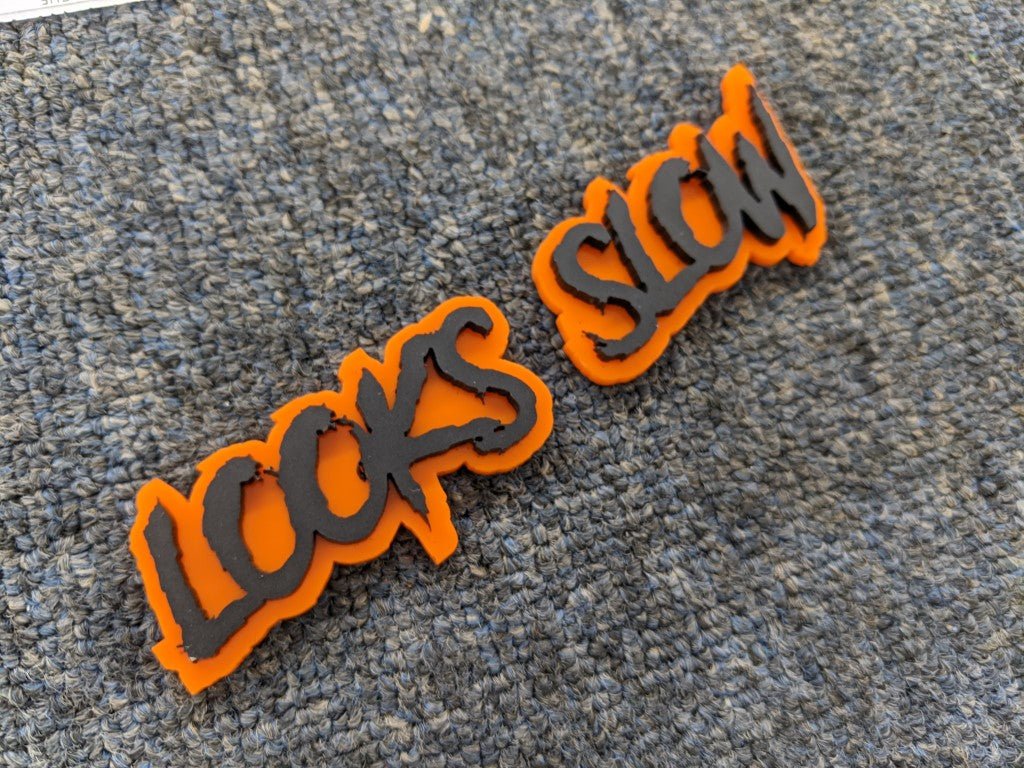 Looks Slow Car Badge - Matte Black on Orange - Aggressive Font - Tape Mounting - Atomic Car Concepts